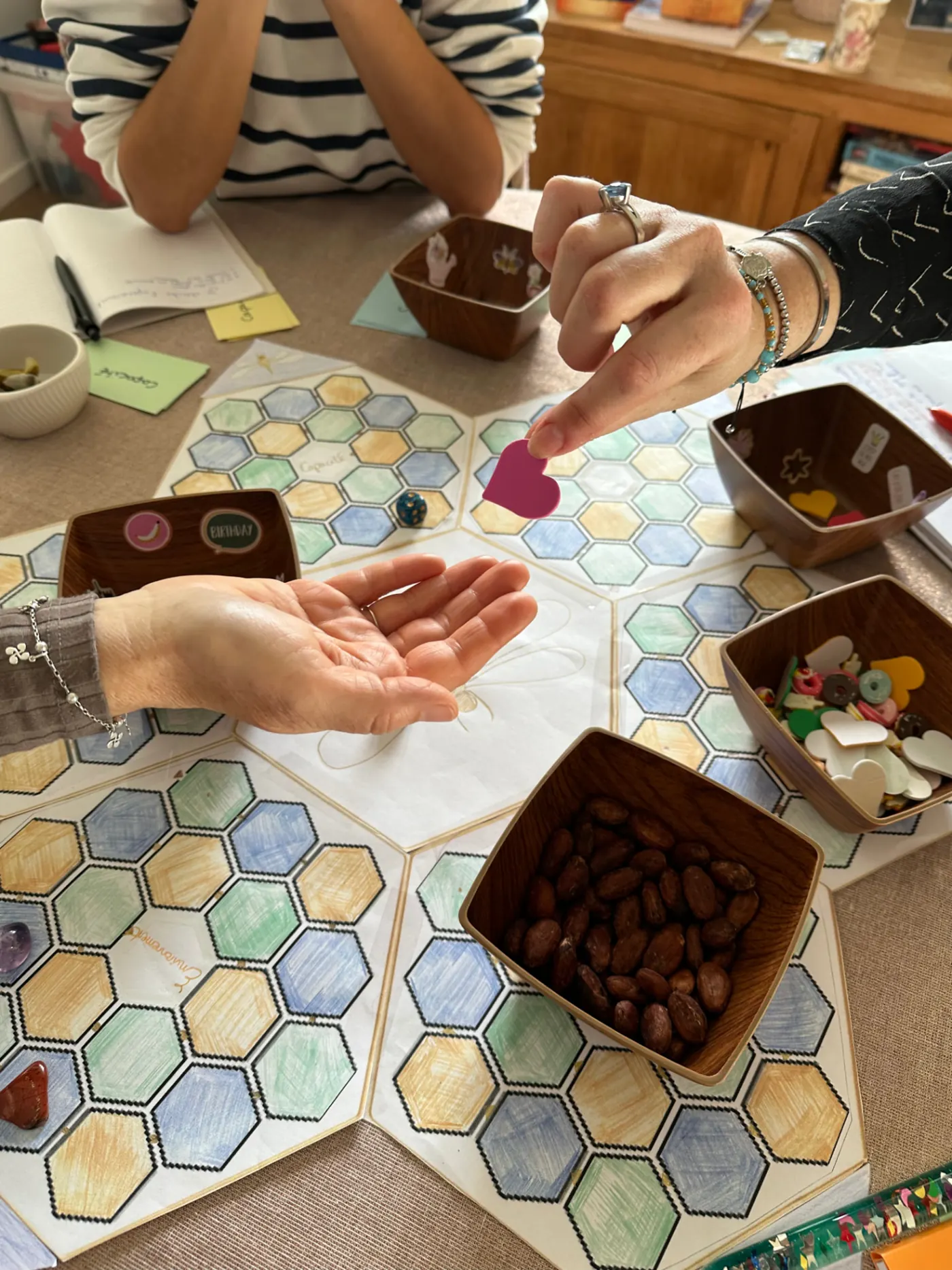 Deux mains échangent un petit cœur au-dessus du plateau du jeu La Pépite® créé par Aurélie Bégo